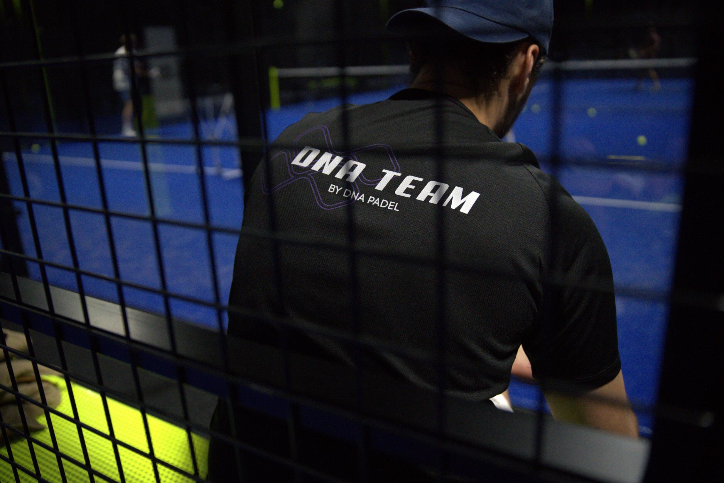 Person wearing a black shirt with 'DNA TEAM' text on a tennis court