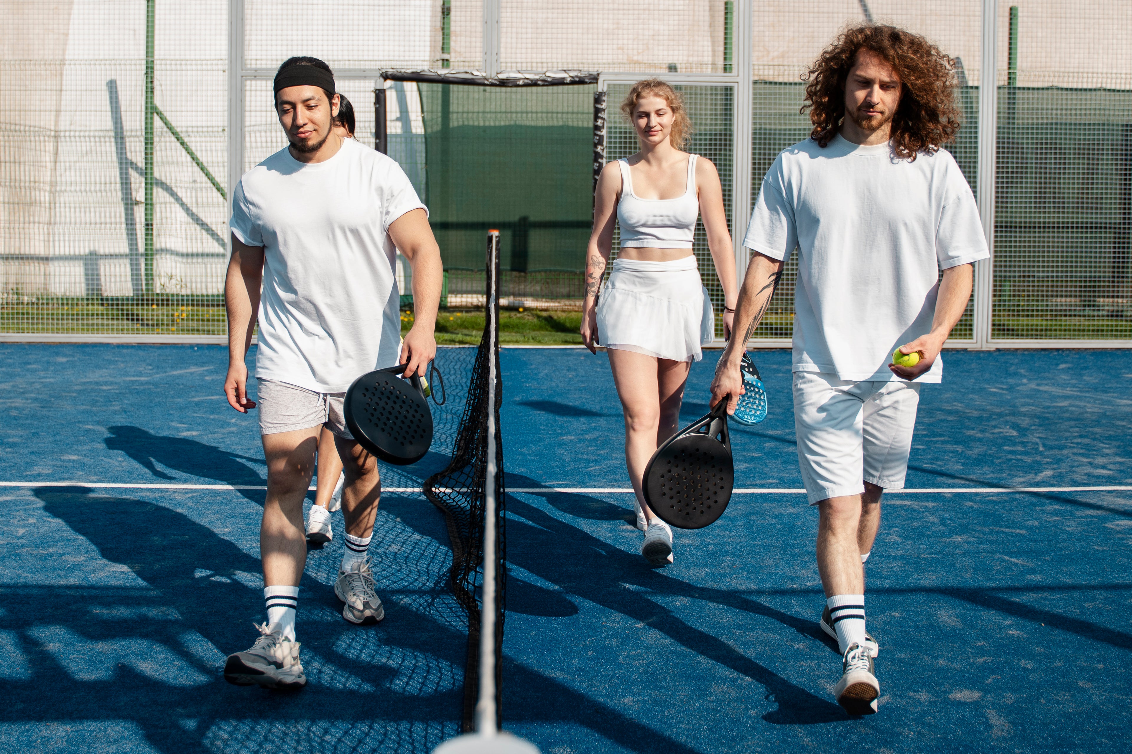 Three people on a tennis court holding tennis rackets and a ball.